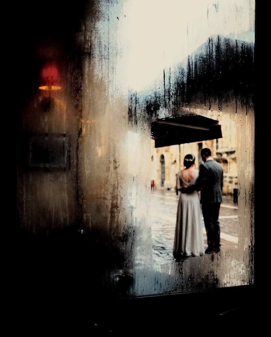 A couple under an awning seen through a misted window, a red lamp behind, developed in Analog Signature