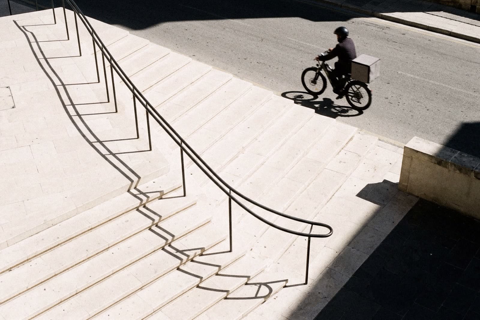 A cyclist and the shadow of a stair rail on pale steps
