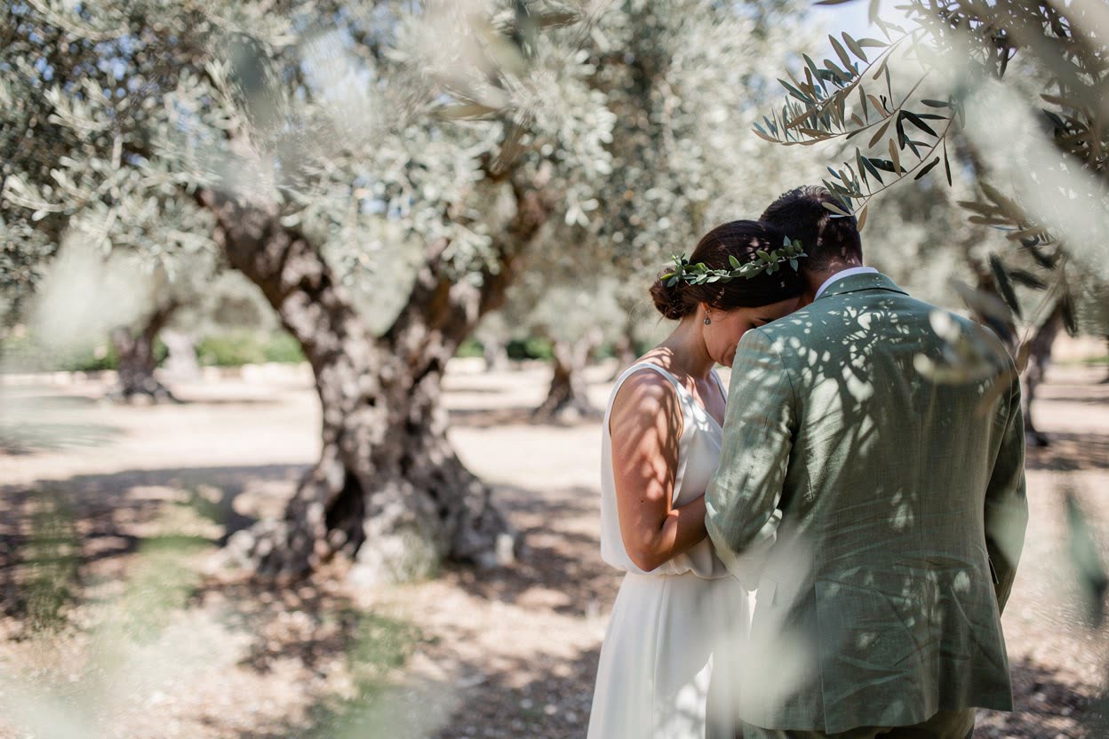 A bride and groom close together in an olive grove, the digital original