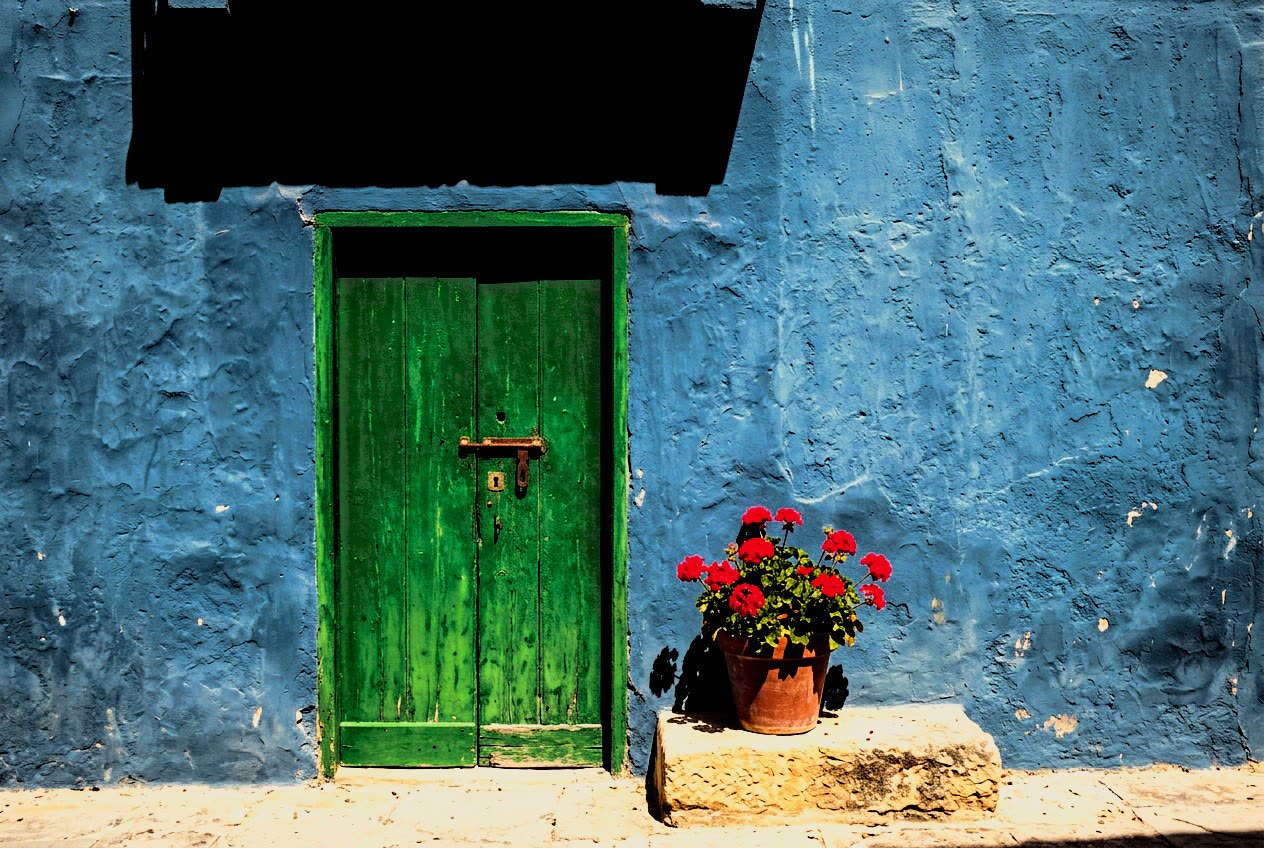 A green door in a blue wall with red geraniums on Gozo, developed in Analog Signature