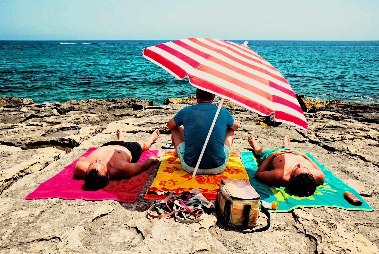 Three sunbathers under a striped umbrella on the rocks at Sliema, developed in Analog Signature